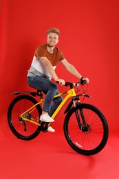 Handsome young man riding bicycle on red background