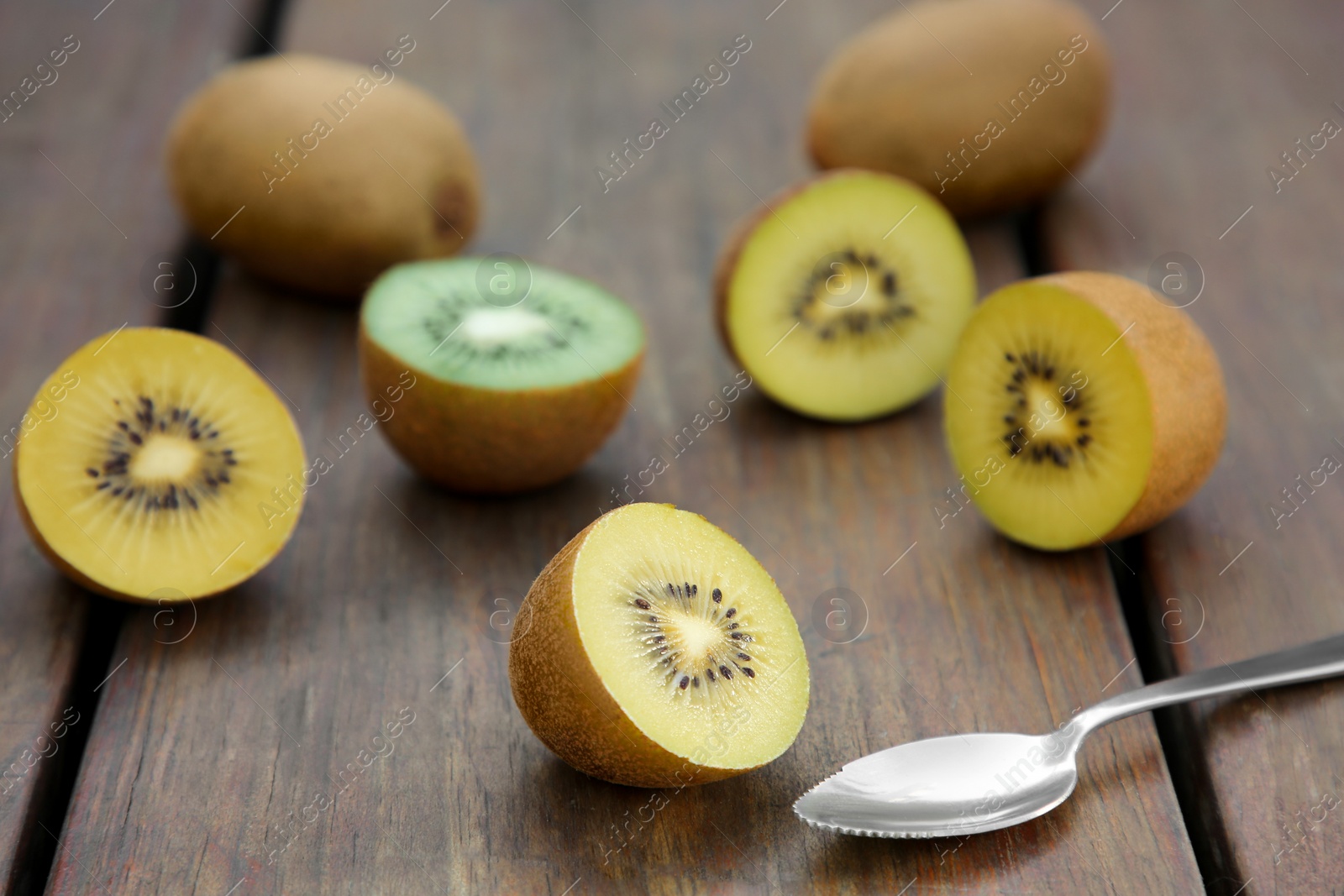 Photo of Spoon with many whole and cut fresh kiwis on wooden table