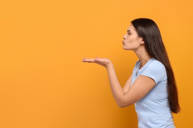 Beautiful young woman blowing kiss on yellow background. Space for text