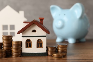 Photo of House models, piggy bank and stacked coins on wooden table against gray background, selective focus