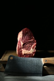 Photo of Piece of raw beef meat and knife on grey table against black background