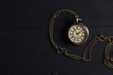 Photo of Pocket clock with chain on black wooden table, top view. Space for text