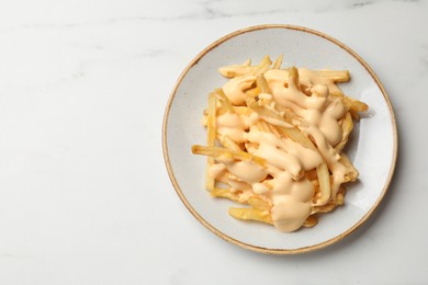 Photo of Delicious French fries with cheese sauce on white marble table, top view. Space for text