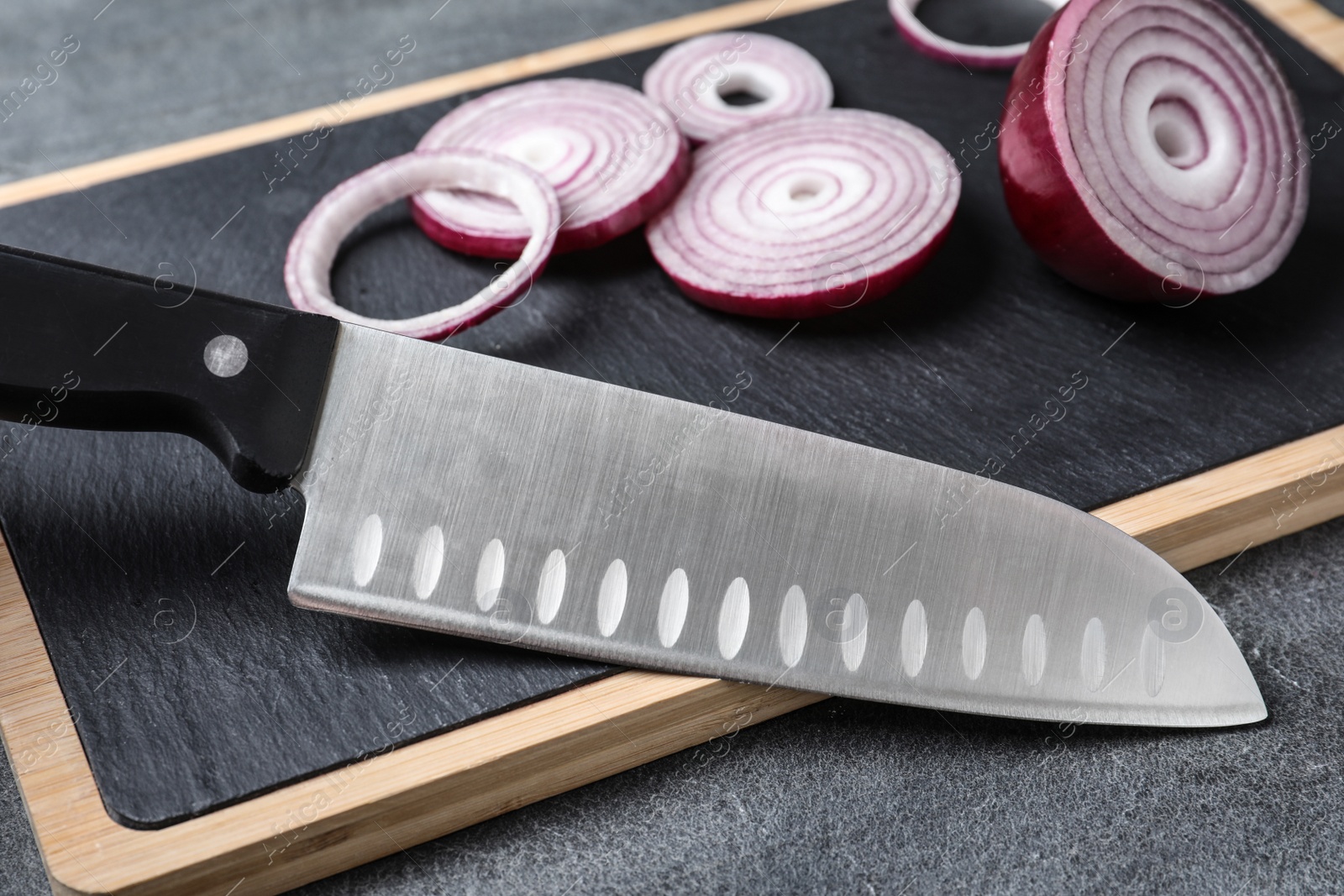 Photo of Board with sharp knife and cut onion on grey background