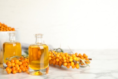 Photo of Natural sea buckthorn oil and fresh berries on white marble table. Space for text