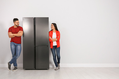 Young couple near refrigerator indoors, space for text