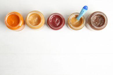 Photo of Healthy baby food in jars on white wooden table, flat lay. Space for text