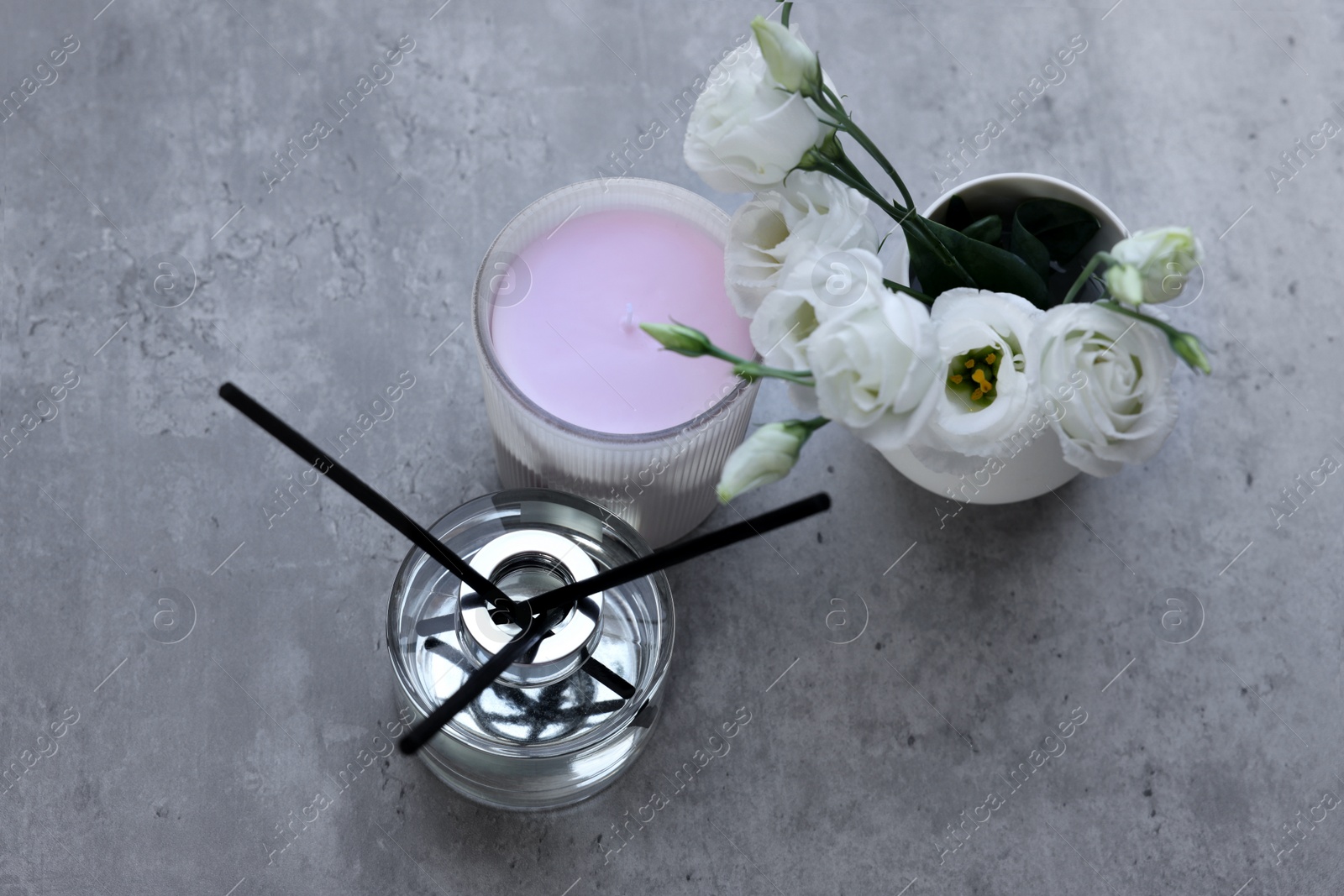 Photo of Reed diffuser, scented candle and eustoma flowers on gray marble table, flat lay