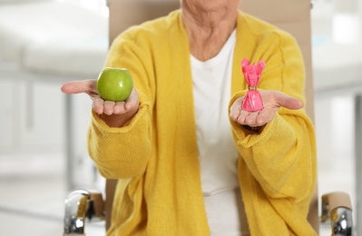 Senior woman with between apple and candy in hospital, closeup. Diabetes diet