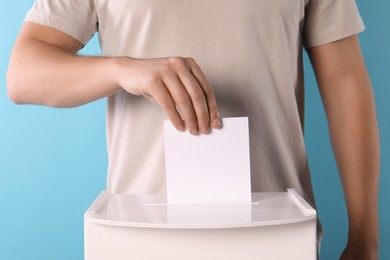 Photo of Man putting his vote into ballot box on light blue background, closeup