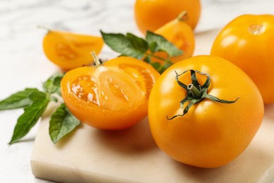 Photo of Fresh ripe yellow tomatoes with leaves on white marble board, closeup
