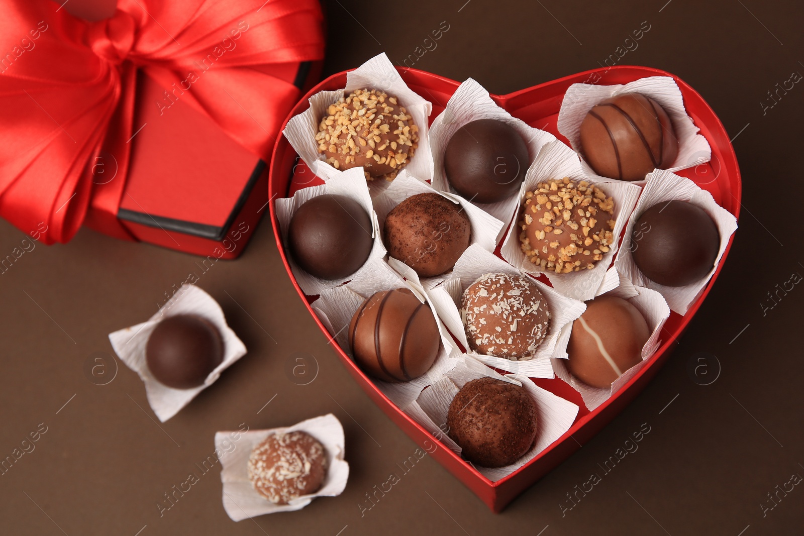 Photo of Heart shaped box with delicious chocolate candies on brown background, flat lay