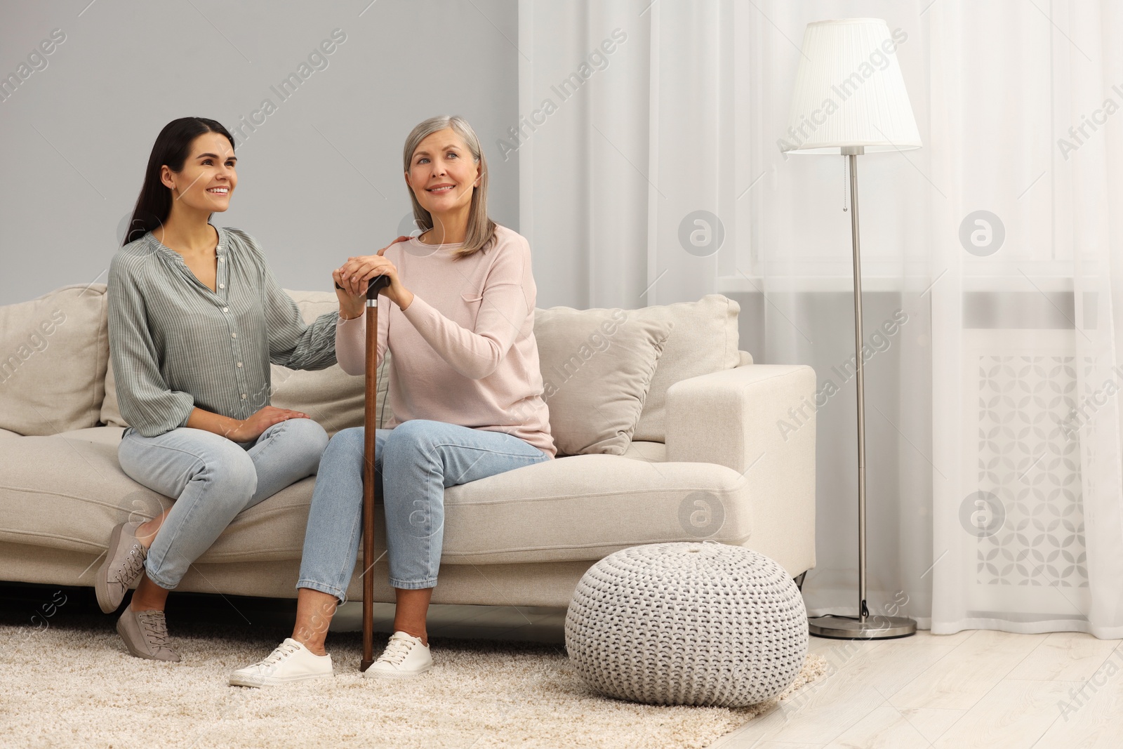 Photo of Mature lady with walking cane and young woman on sofa at home