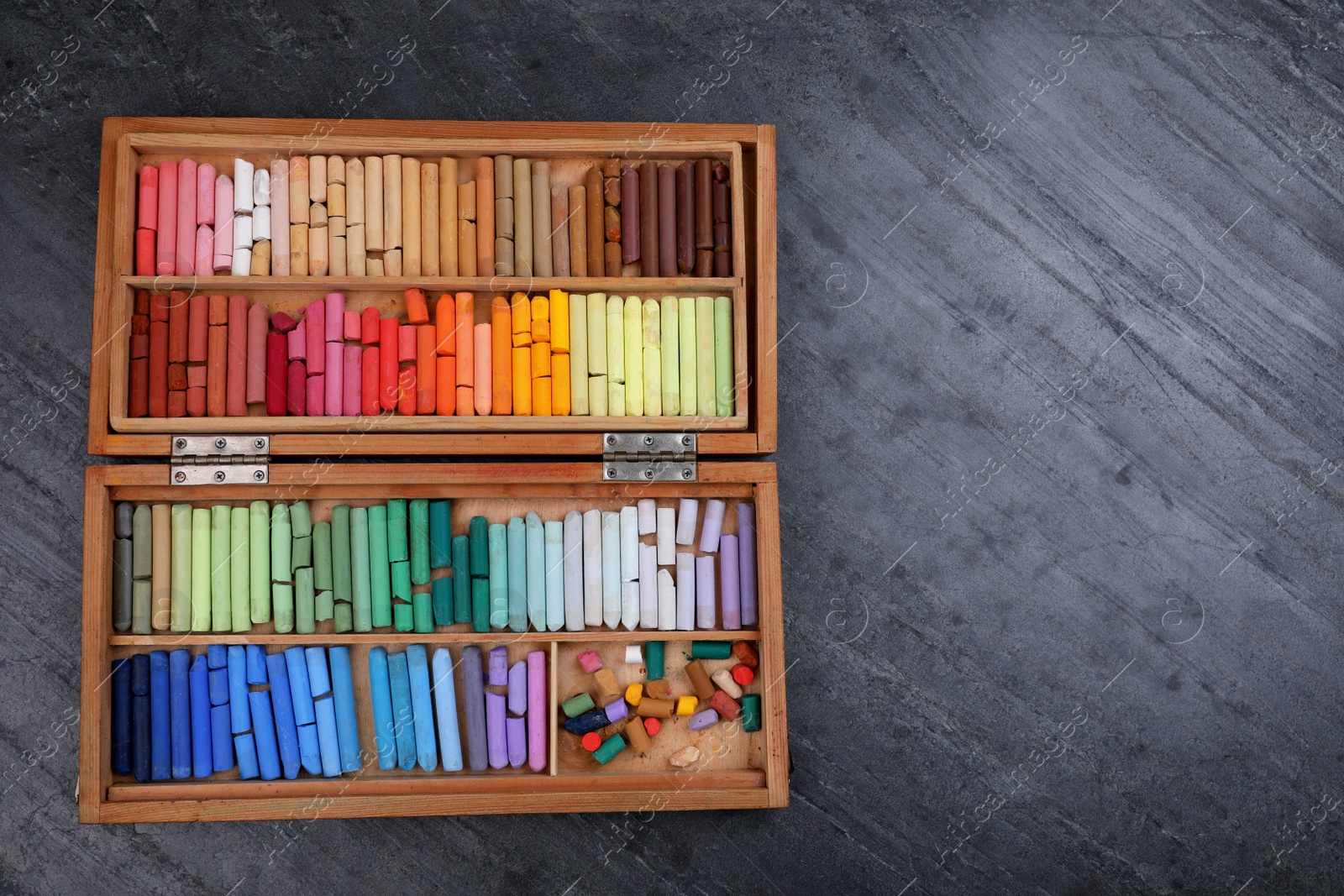 Photo of Set of colorful pastels in wooden box on grey stone table, top view with space for text. Drawing materials