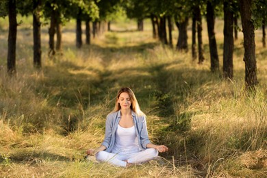 Photo of Young woman meditating in forest on sunny day