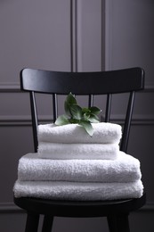 Stacked soft towels and green leaves on black chair indoors