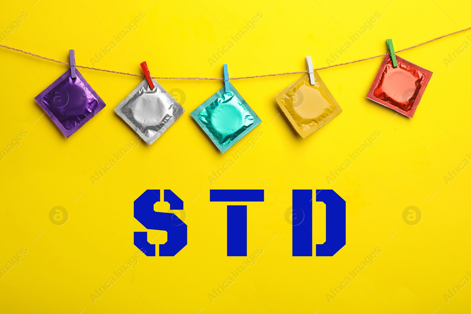 Image of Colorful condoms hanging on clothesline and abbreviation STD against yellow background 