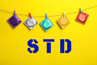 Colorful condoms hanging on clothesline and abbreviation STD against yellow background 