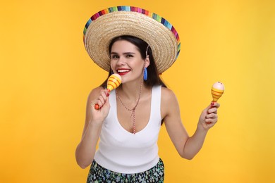 Young woman in Mexican sombrero hat with maracas on yellow background