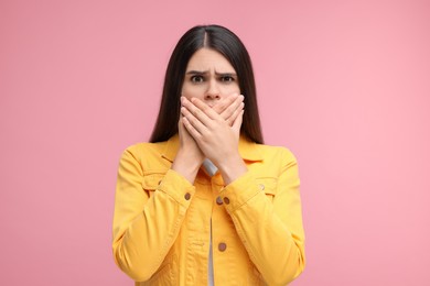 Photo of Embarrassed woman covering mouth with hands on pink background