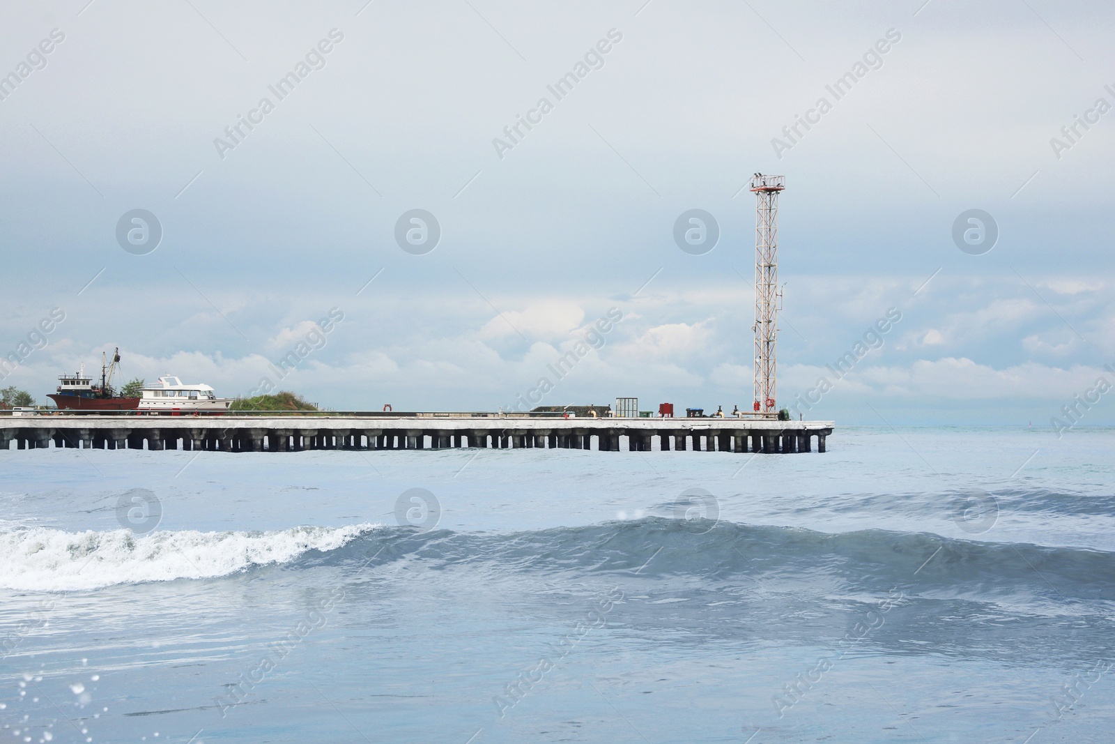 Photo of Picturesque view of pier in sea with waves on cloudy day