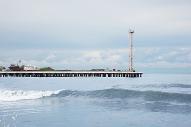 Photo of Picturesque view of pier in sea with waves on cloudy day