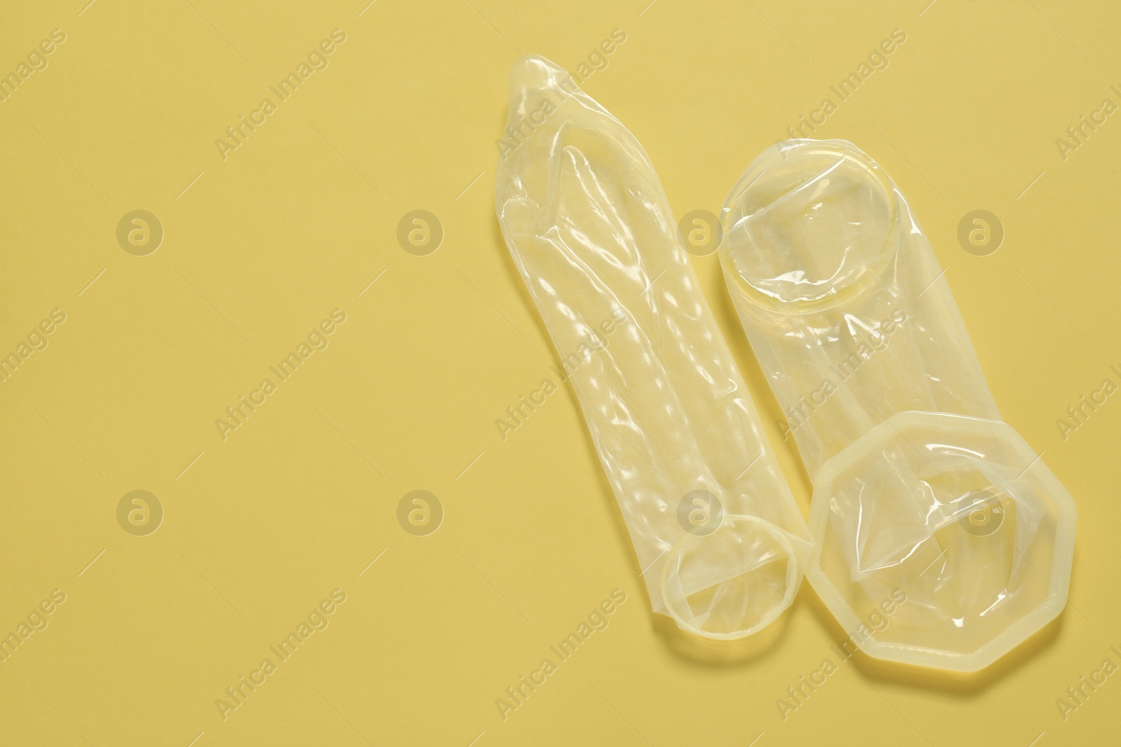Photo of Unrolled female, male condoms on yellow background, flat lay with space for text. Safe sex