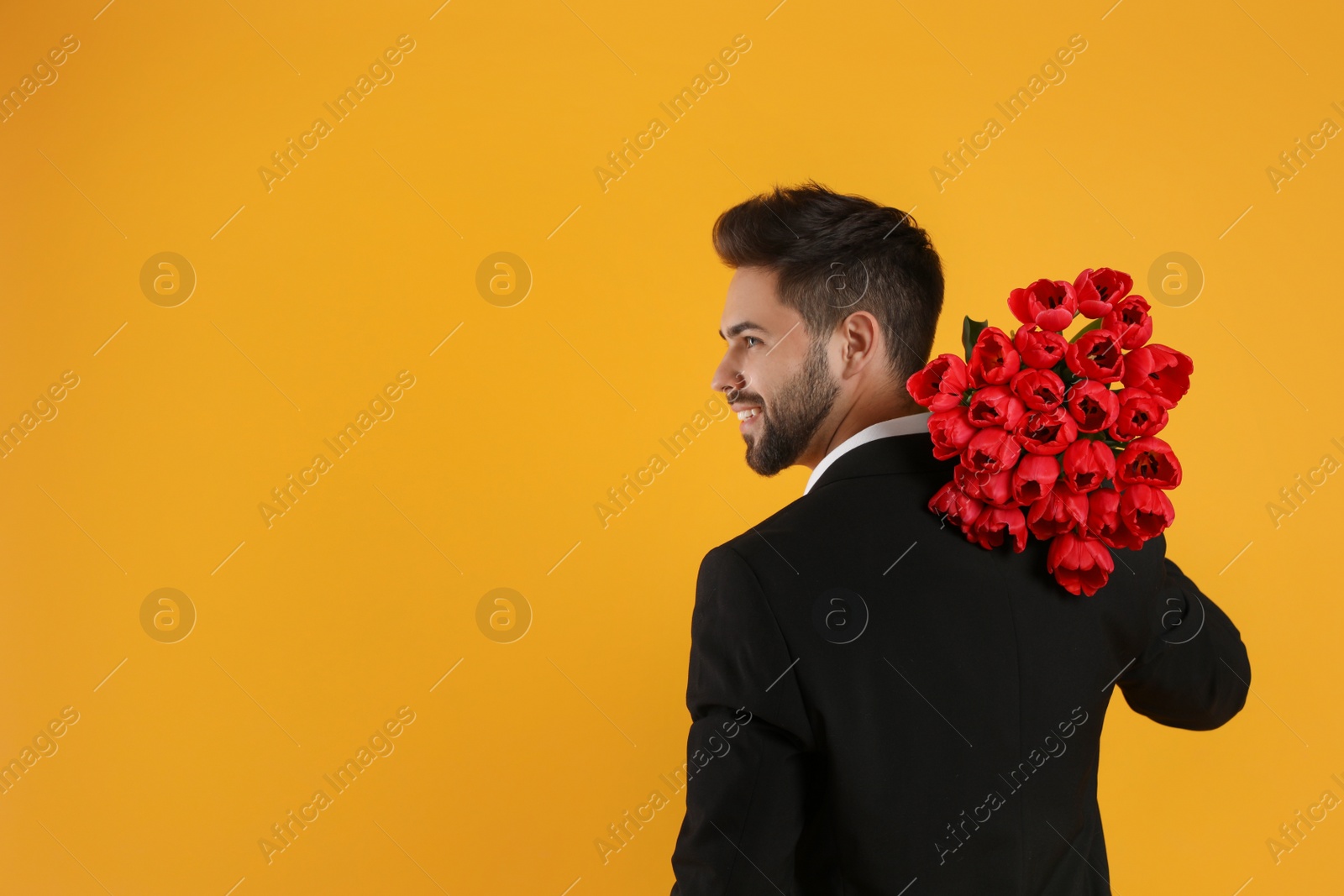 Photo of Happy man with red tulip bouquet on yellow background, space for text. 8th of March celebration