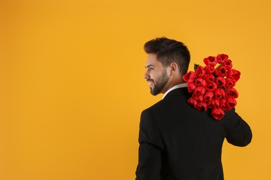 Happy man with red tulip bouquet on yellow background, space for text. 8th of March celebration