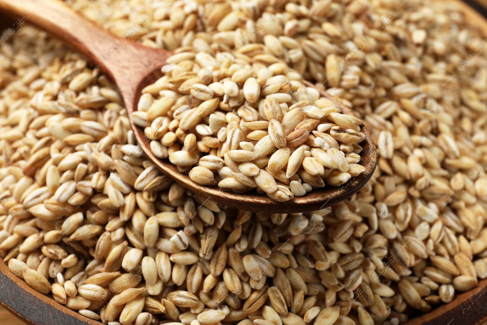 Photo of Wooden spoon with dry pearl barley, closeup