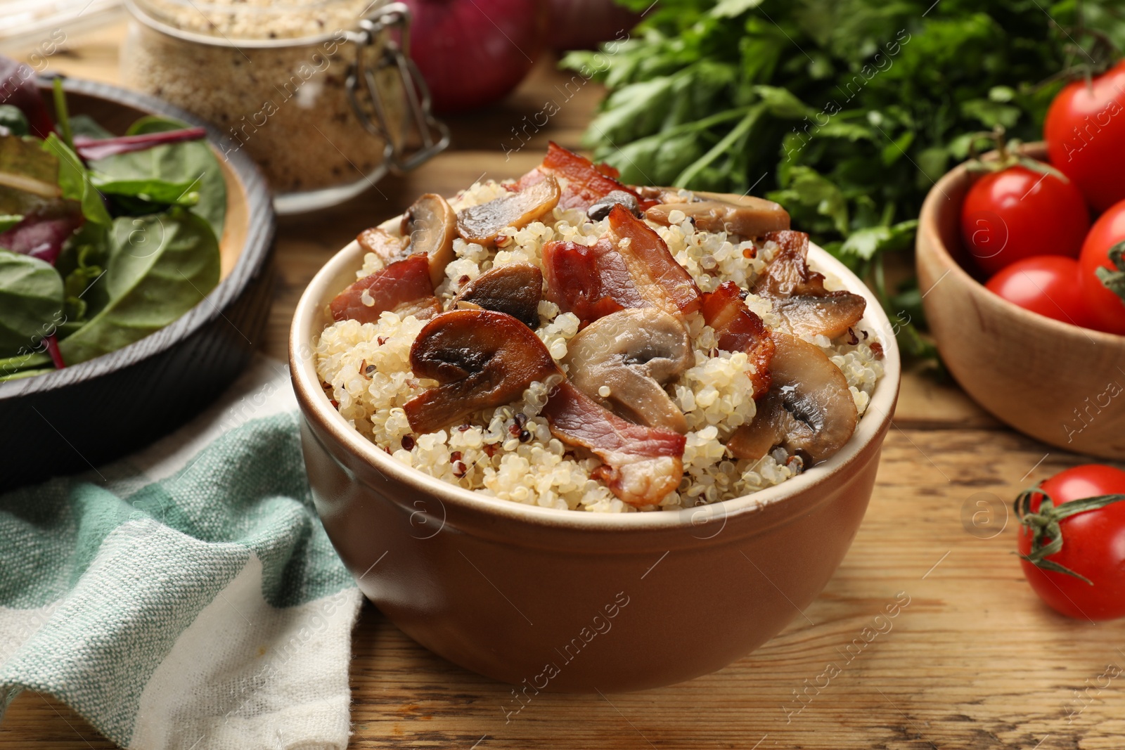 Photo of Tasty quinoa porridge with fried bacon and mushrooms in bowl on wooden table, closeup