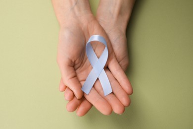 Photo of International Psoriasis Day. Woman with light blue ribbon as symbol of support on green background, top view