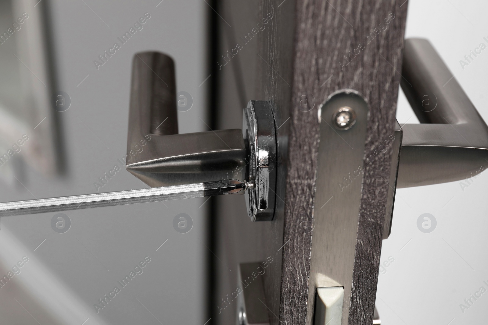 Photo of Repairing door handle with screwdriver indoors, closeup