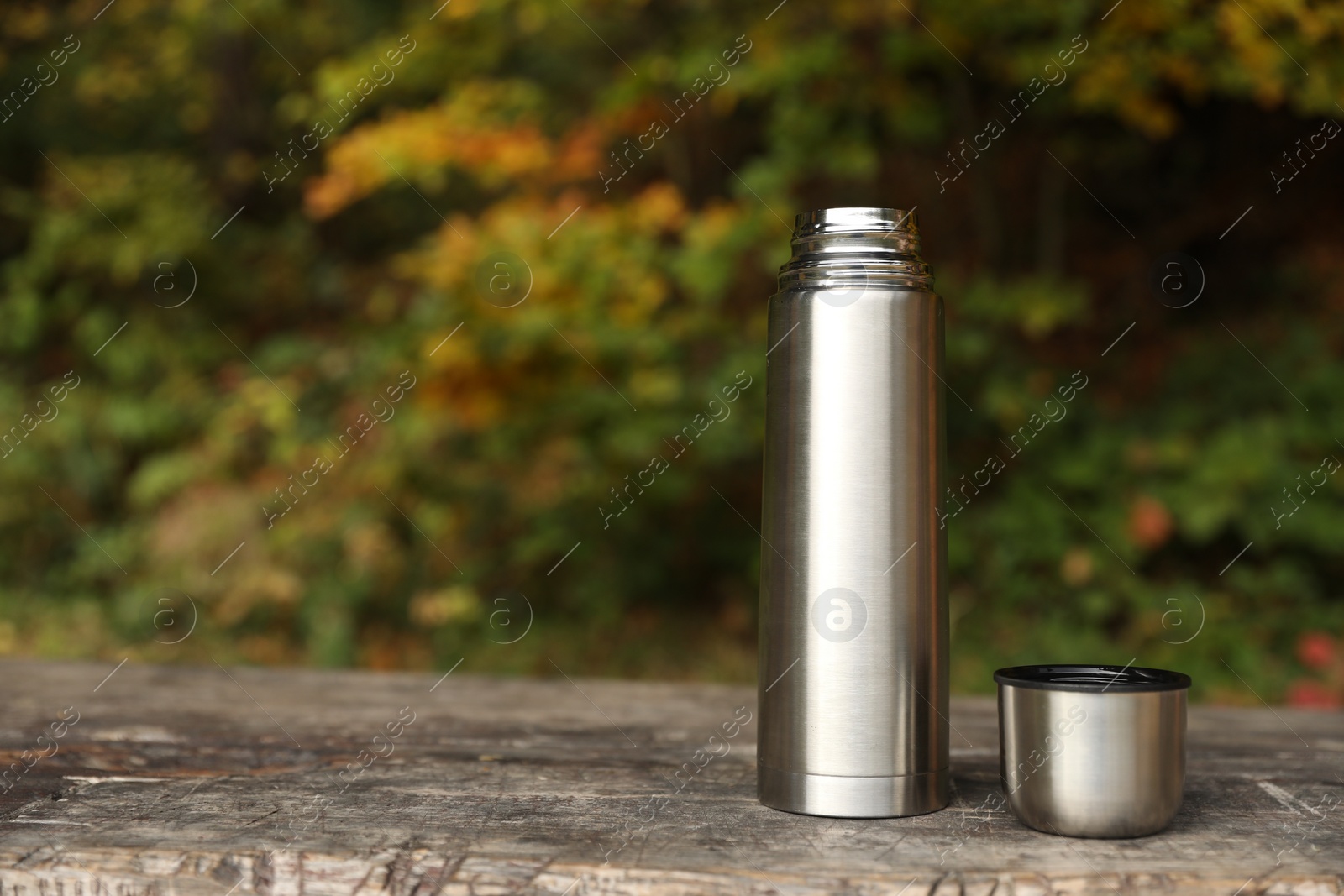 Photo of Metallic thermos and cup lid on wooden bench outdoors, space for text