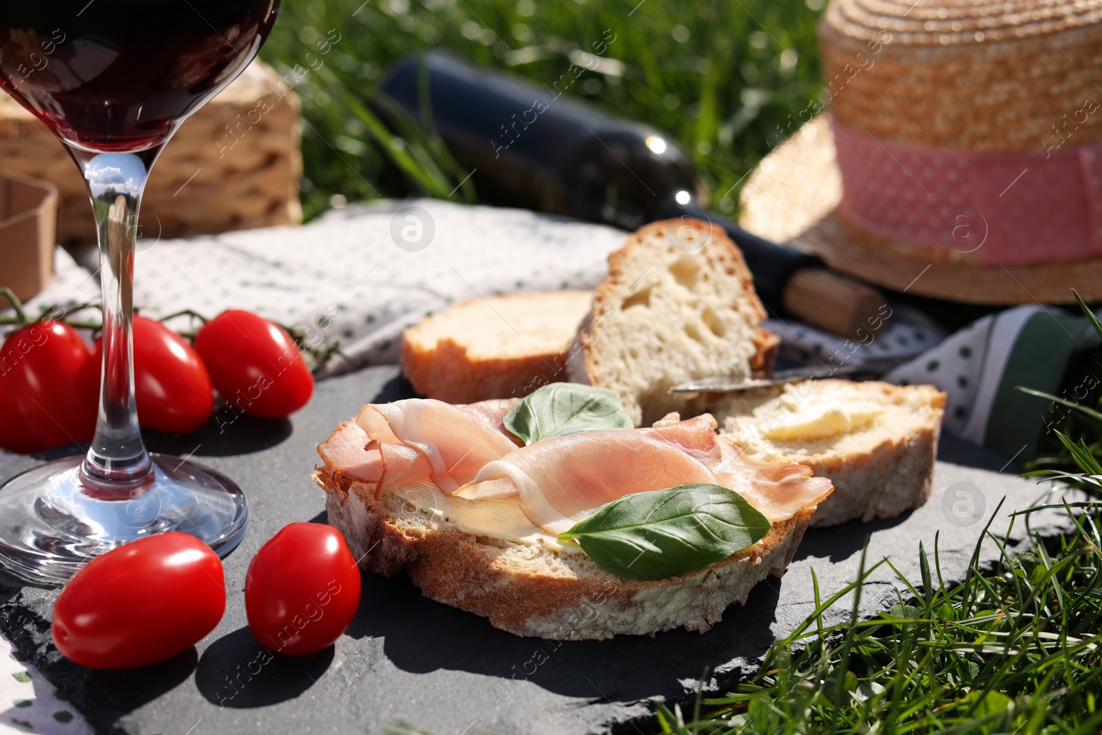 Photo of Blanket with wine and snacks for picnic on green grass, closeup