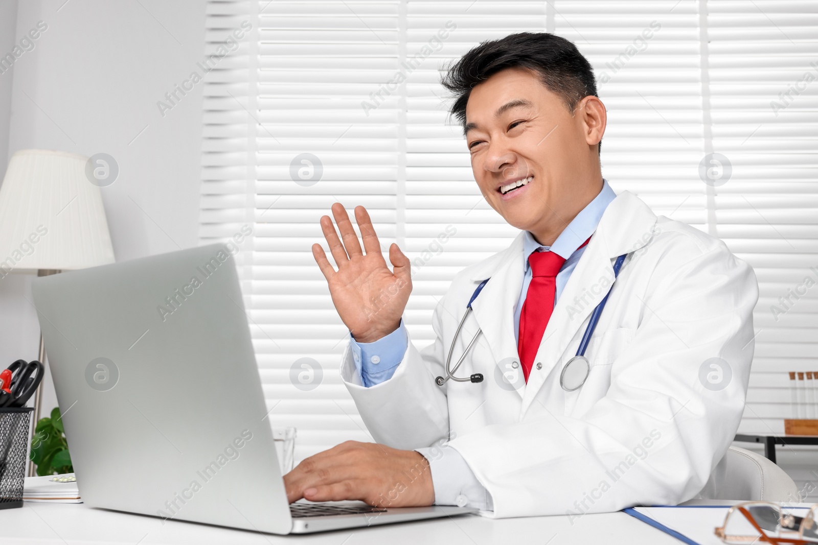 Photo of Happy doctor with laptop consulting patient at white desk in clinic. Online medicine