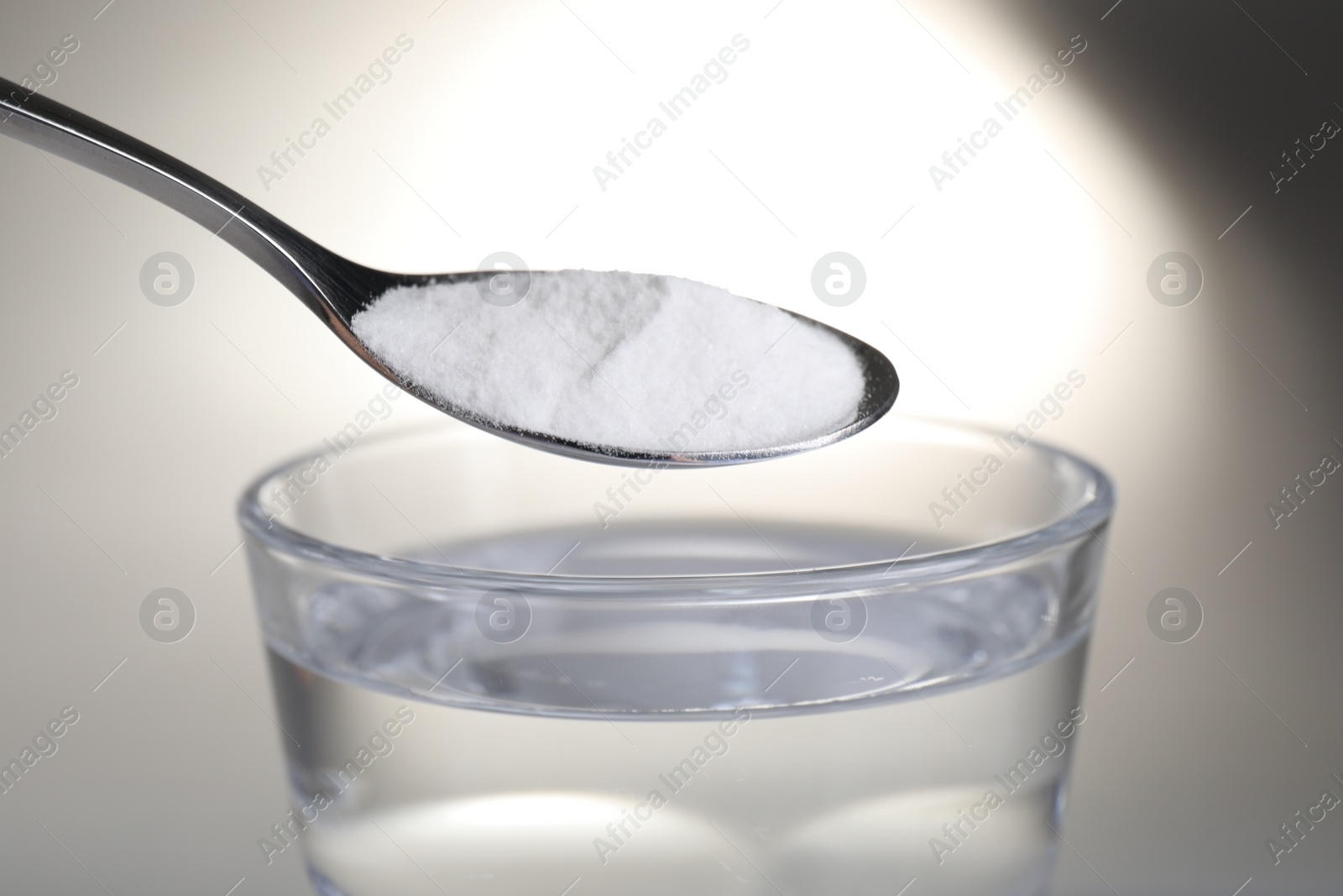 Photo of Spoon with baking soda over glass of water on light background, closeup