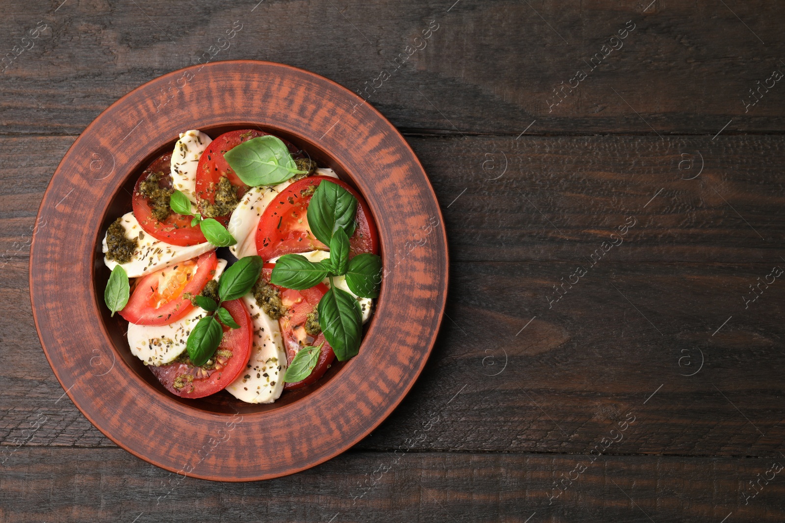 Photo of Plate of delicious Caprese salad with pesto sauce on wooden table, top view. Space for text