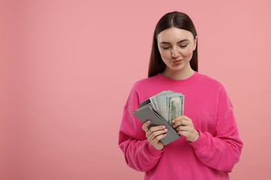 Photo of Woman putting money into wallet on pink background, space for text