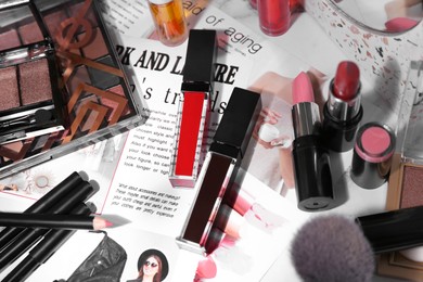 Photo of Bright lip glosses among different cosmetic products and fashion magazine on table