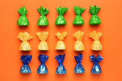 Photo of Many candies in colorful wrappers on orange background, flat lay