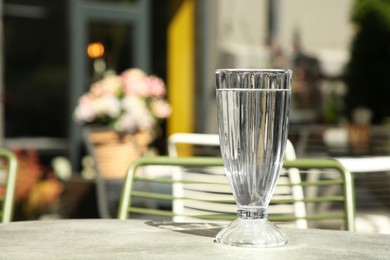 Photo of Glass of fresh water on light grey table outdoors. Space for text