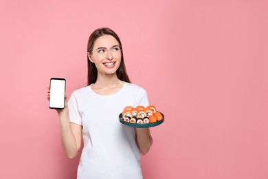 Photo of Happy young woman with plate of sushi rolls and smartphone on pink background. Space for text