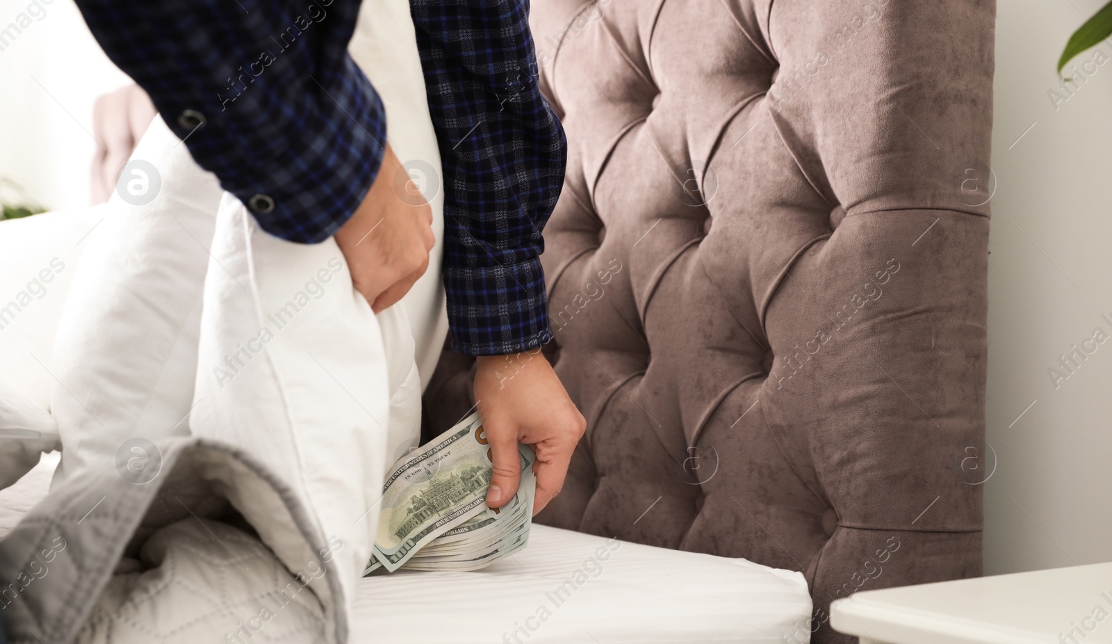 Photo of Man hiding dollar banknotes under blanket in bedroom, closeup. Money savings