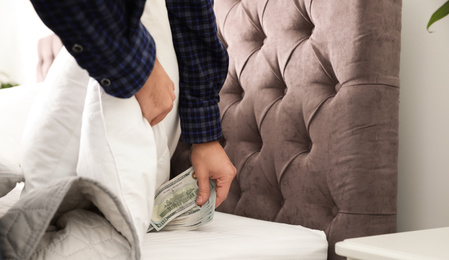 Man hiding dollar banknotes under blanket in bedroom, closeup. Money savings