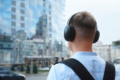 Photo of Man in headphones listening to music outdoors, back view. Space for text