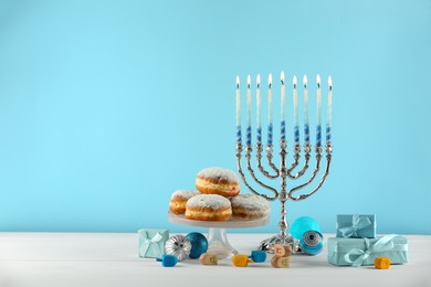 Composition with Hanukkah menorah, dreidels and gift boxes on white table against light blue background. Space for text