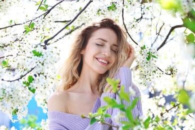 Attractive young woman posing near blossoming tree on sunny spring day