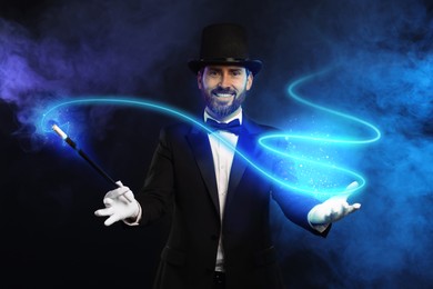Magic and sorcery. Magician with wand and fantastic light in smoke on dark background