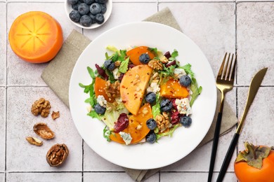 Delicious persimmon salad, fork and knife on tiled surface, flat lay